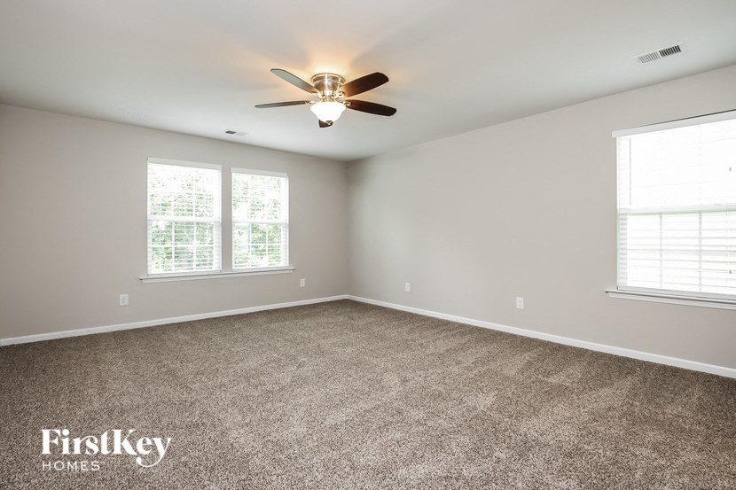 A spacious room with a ceiling fan and two windows.