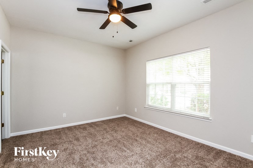 the spacious living room with carpeted flooring and a ceiling fan