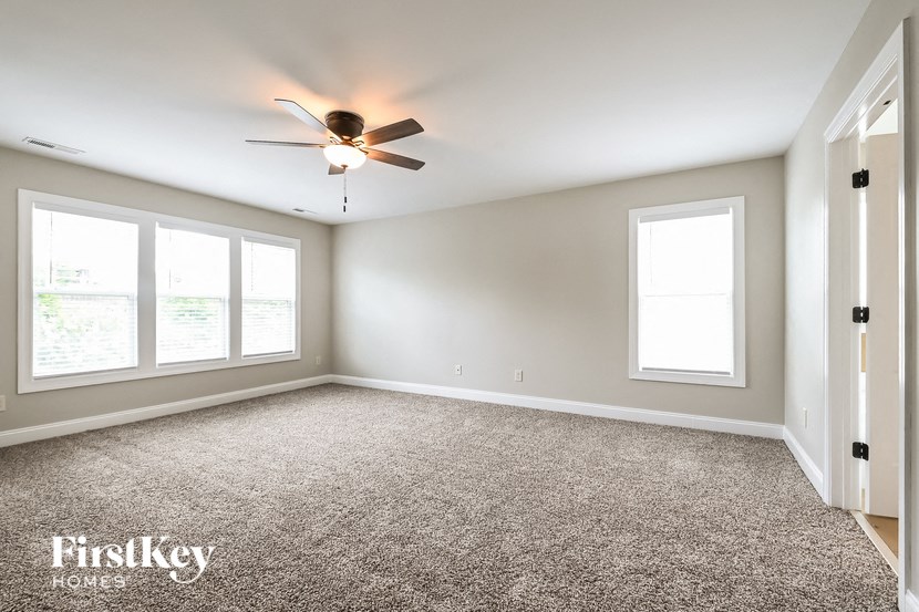 an empty living room with a ceiling fan and three windows