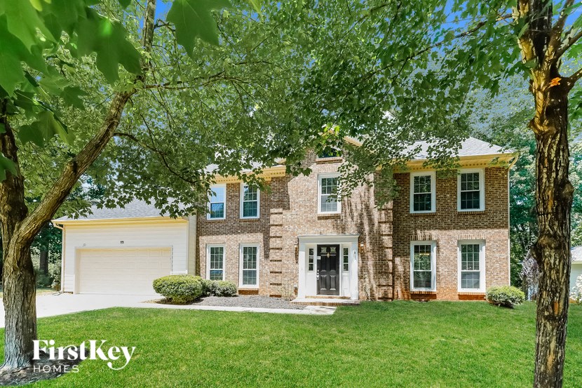 A brick house with a white door and windows is surrounded by trees.