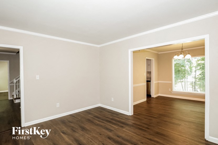 A room with wooden floors and white walls, with a doorway leading to another room.