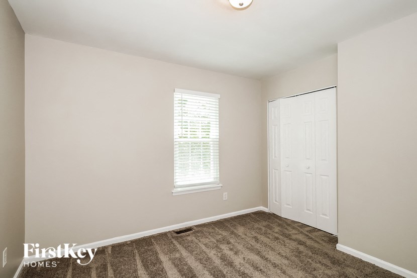 A room with a carpeted floor, a window with blinds, and a door.