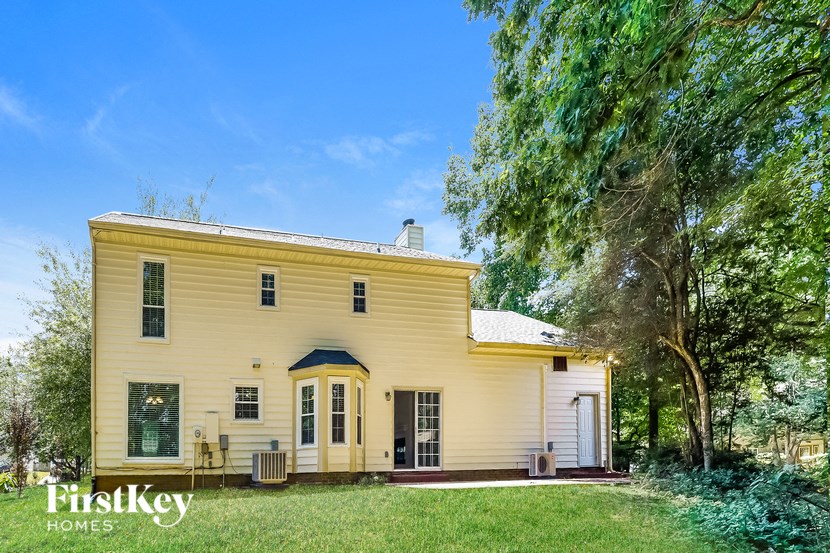 A yellow house with a porch and a tree in front of it.
