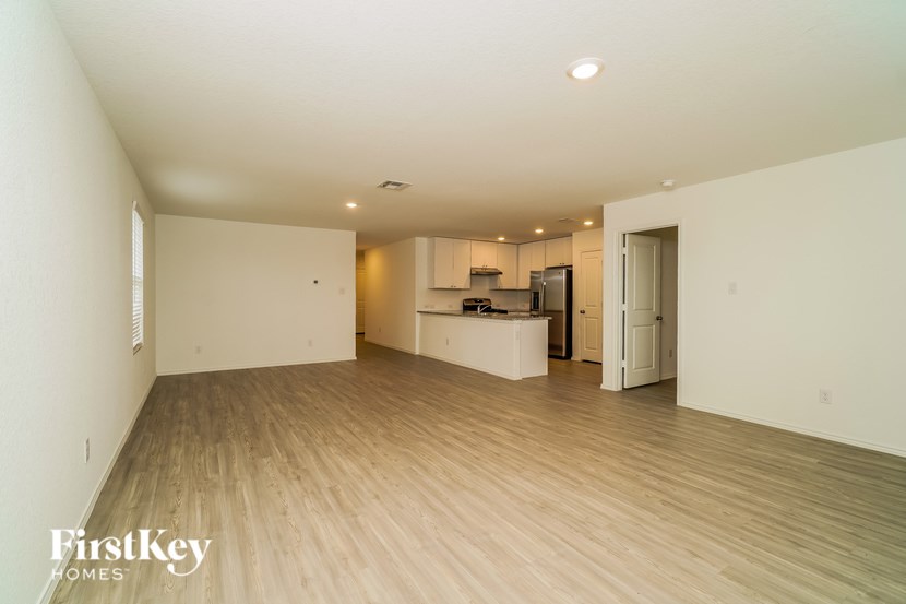 A spacious empty room with wooden flooring and a kitchen area in the background.