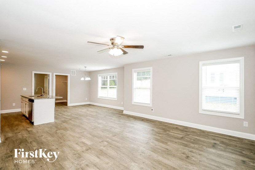 an empty living room with a ceiling fan and a kitchen