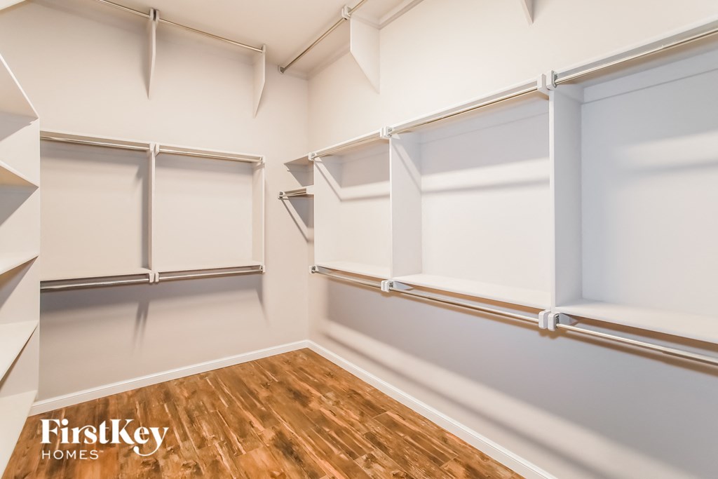 a walk in closet with white walls and wood floors