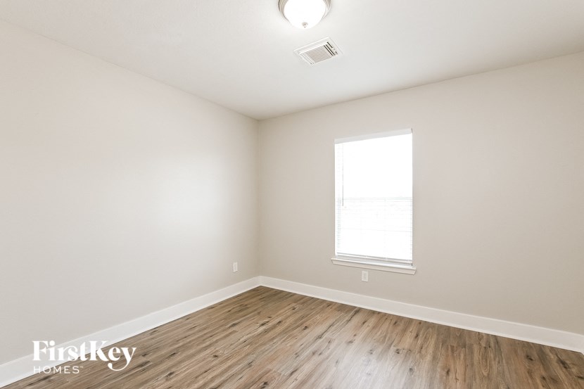a bedroom with white walls and wood floors and a window