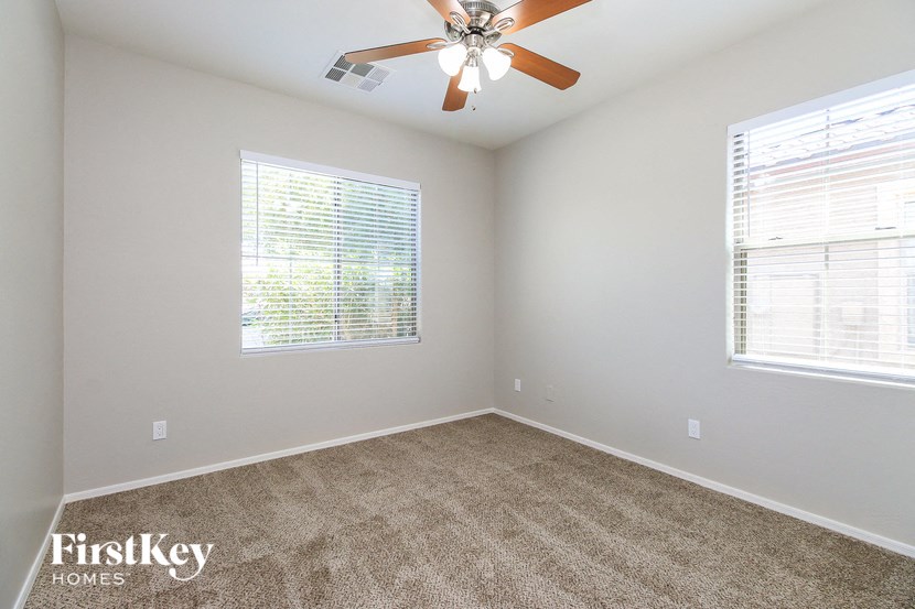 an empty bedroom with a ceiling fan and two windows