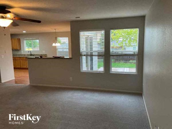 an empty living room with a kitchen and a ceiling fan