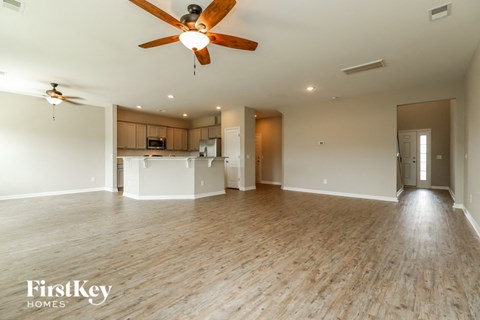an empty living room with a ceiling fan and a kitchen