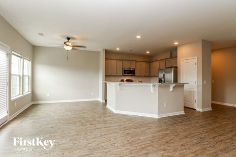 an empty living room with a kitchen and a ceiling fan