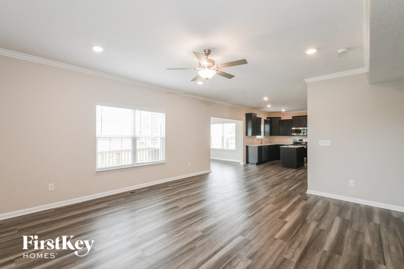 an empty living room with a ceiling fan and a kitchen