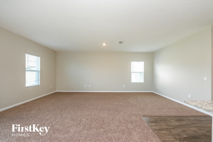 A spacious room with a carpeted floor and two windows.