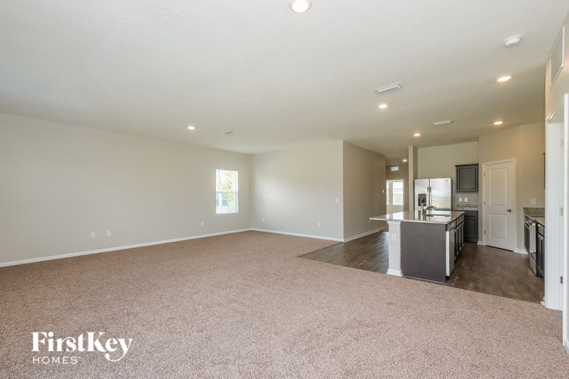 A spacious empty room with a kitchen area in the background.