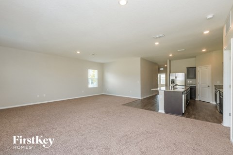 A spacious empty room with a kitchen area in the background.