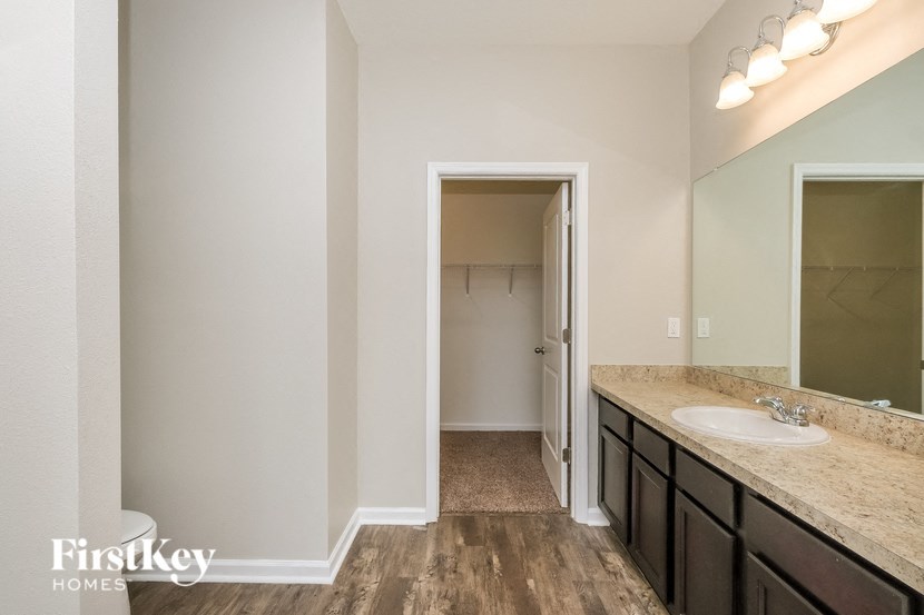 A bathroom with a wooden floor and a mirror above the sink.