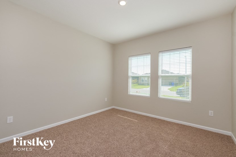 A room with a carpeted floor and two windows.