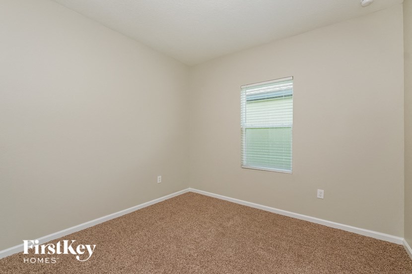 A room with a carpeted floor and a window with blinds.