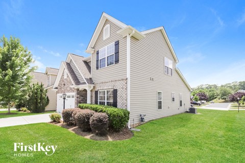 a beige house with a lawn and shrubs in front
