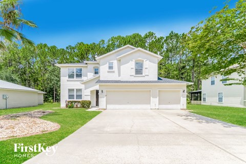 A white house with a garage is surrounded by greenery and has a clear blue sky above it.