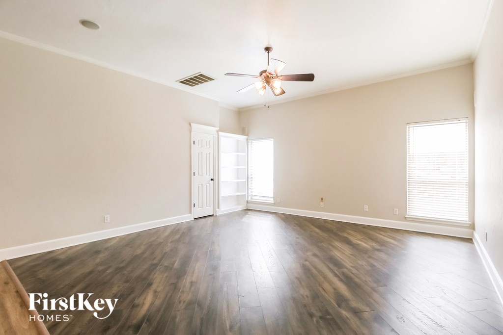 A spacious room with wooden floors and a ceiling fan.