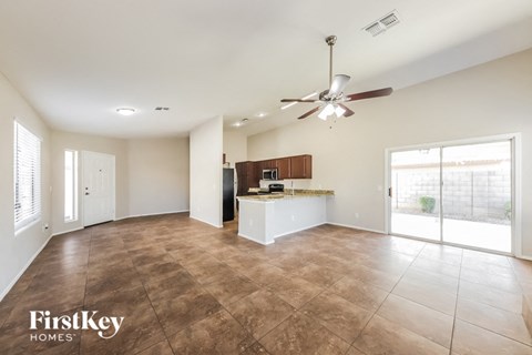 an empty living room with a kitchen and a ceiling fan