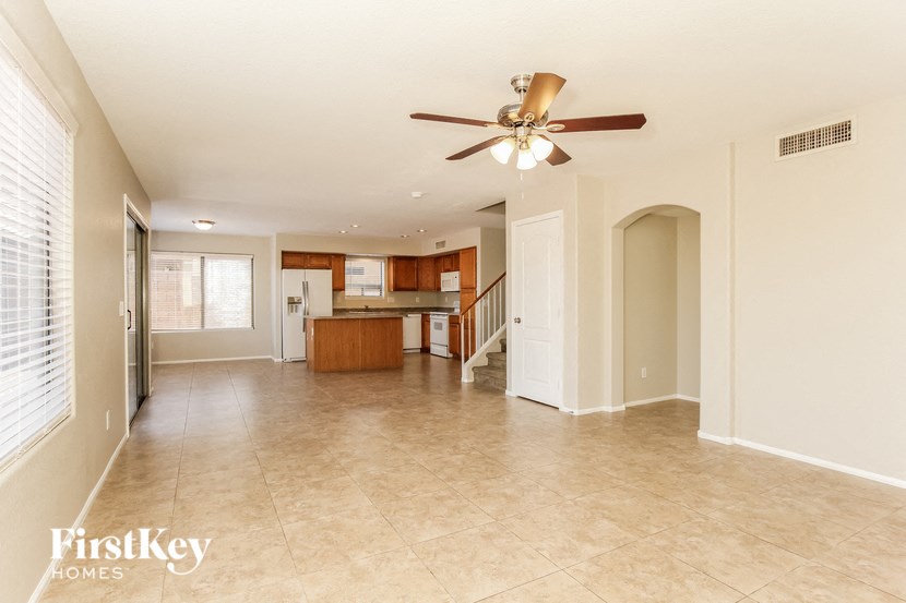 an empty living room with a ceiling fan and a kitchen