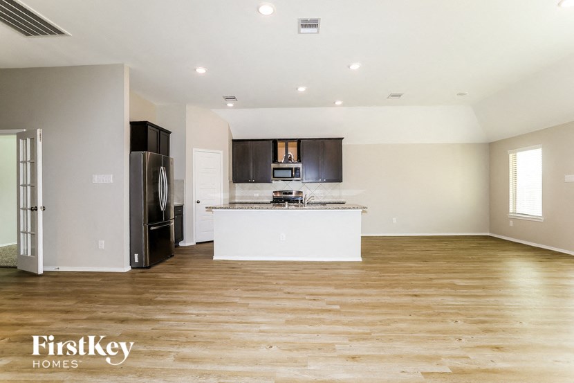A spacious kitchen with wooden floors and a refrigerator on the left.