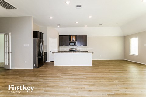 A spacious kitchen with wooden floors and a refrigerator on the left.