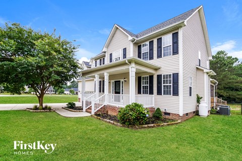 a white house with a porch and a tree in the yard
