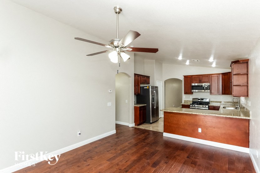 an empty living room with a kitchen and a ceiling fan