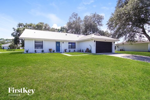 A white house with a black garage door is surrounded by a grassy lawn.