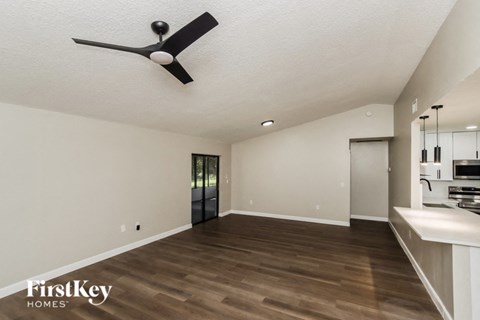 A spacious room with a fan and a kitchen area in the background.