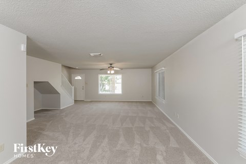 A spacious room with a carpeted floor and a staircase on the left side.