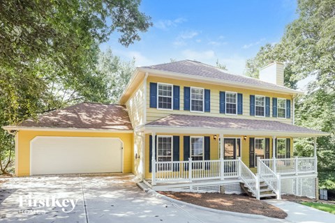 a yellow house with a porch and a white fence