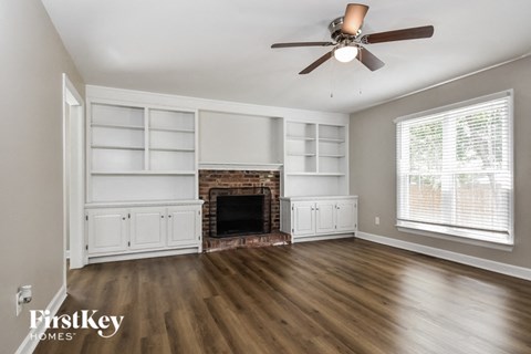 a living room with a fireplace and white shelves and a ceiling fan