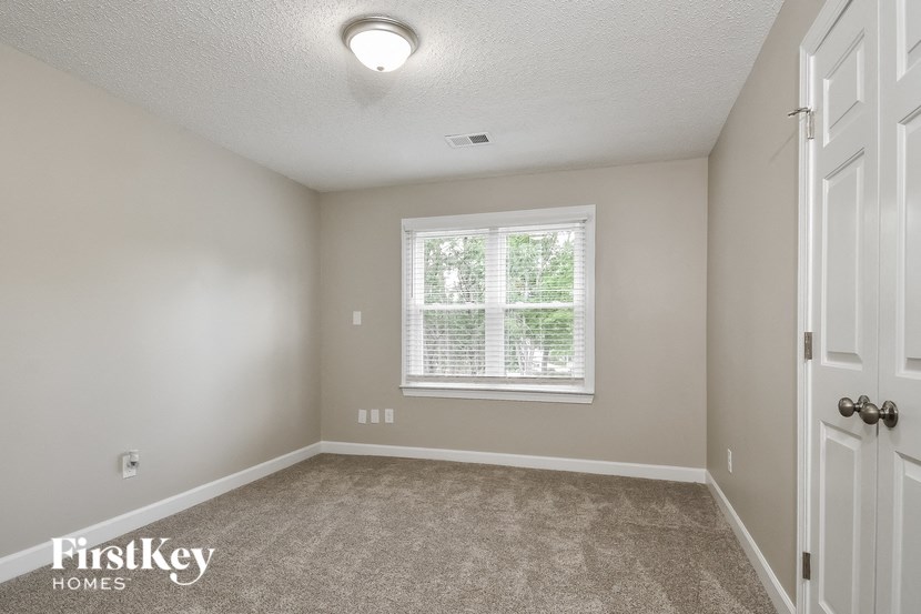 the bedroom of a home with a large window and carpeted flooring