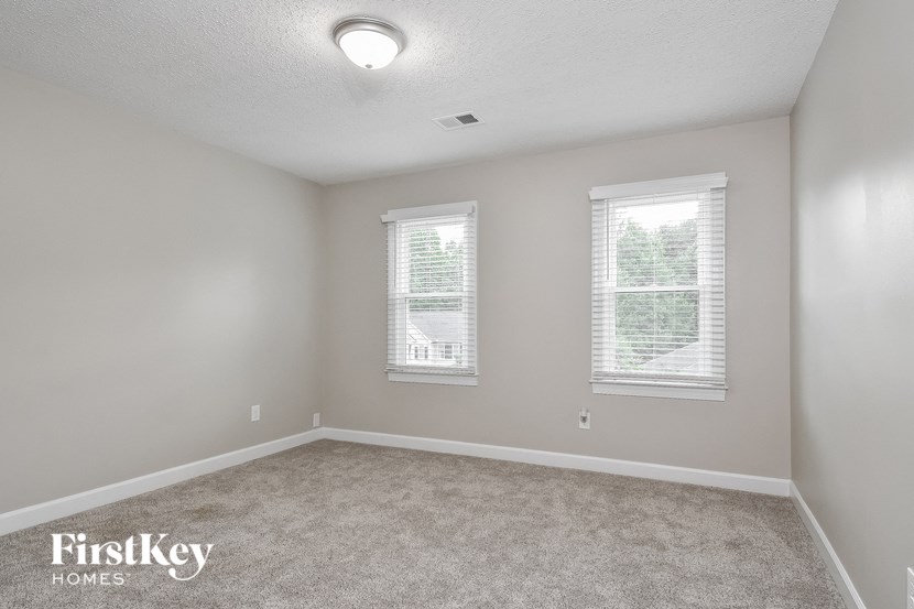 an empty bedroom with two windows and a carpeted floor