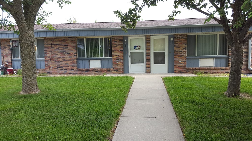 the front of a brick building with a sidewalk and grass