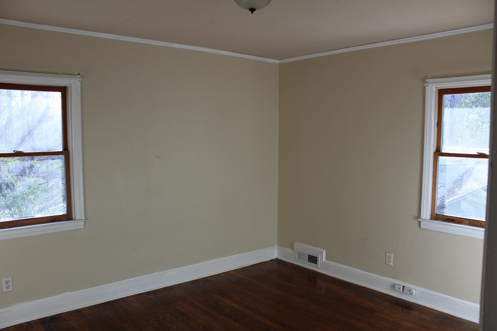 an empty room with wooden floors and two windows