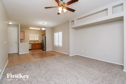 an empty living room with a ceiling fan and a kitchen