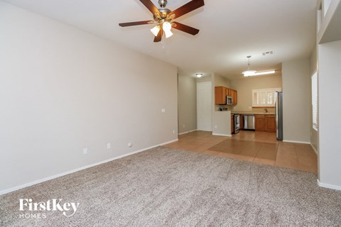 an empty living room with a ceiling fan and a kitchen