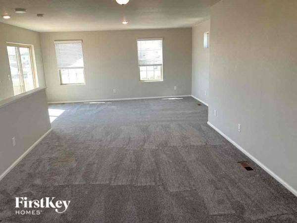 an empty living room with gray carpet and two windows