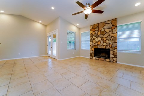 an empty living room with a stone fireplace and tile flooring