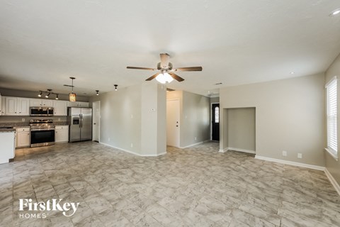 A spacious living room with a fan and a kitchen in the background.