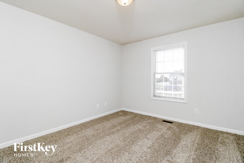 a bedroom with white walls and carpet and a window