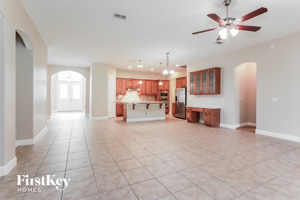 A spacious living room with a kitchen in the background and a fan on the ceiling.