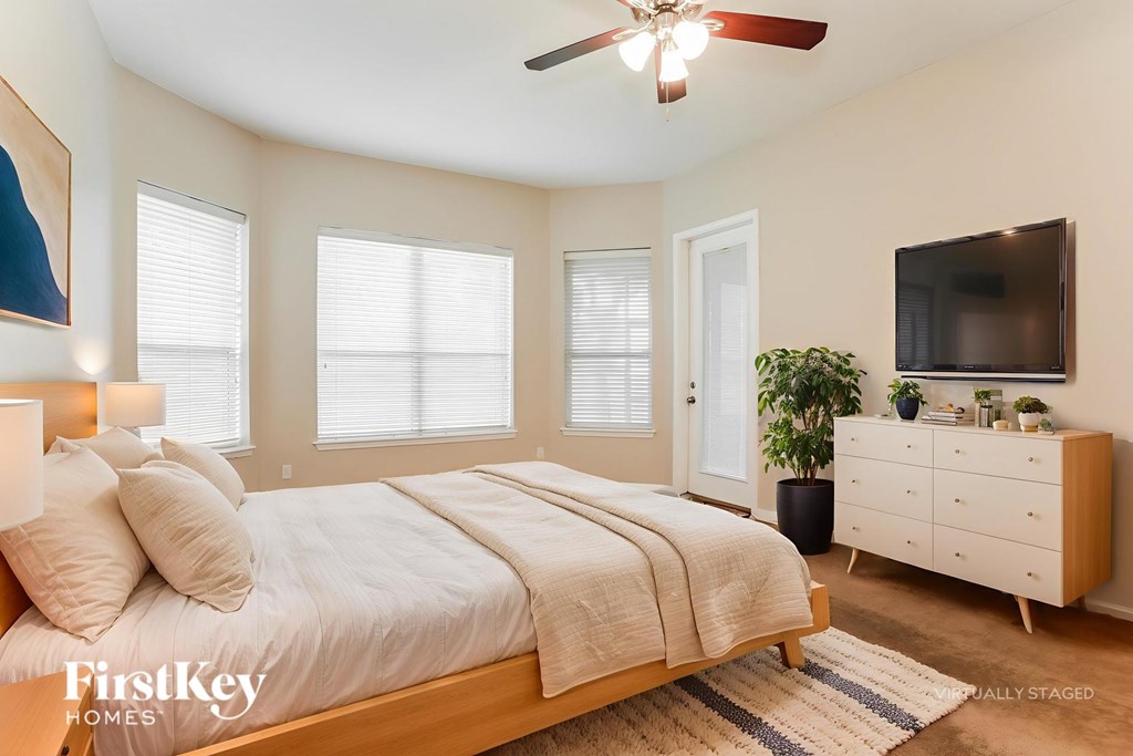 A bedroom with a bed, a ceiling fan, and a TV mounted on the wall.