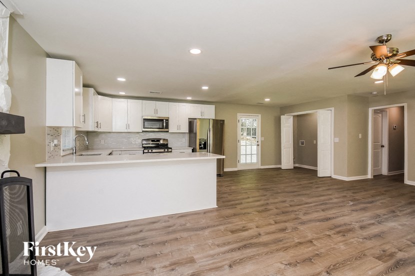 an empty living room with a kitchen and a ceiling fan