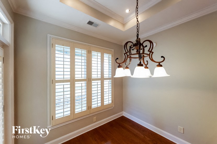 A chandelier hangs in a well-lit room with a window covered in white shutters.